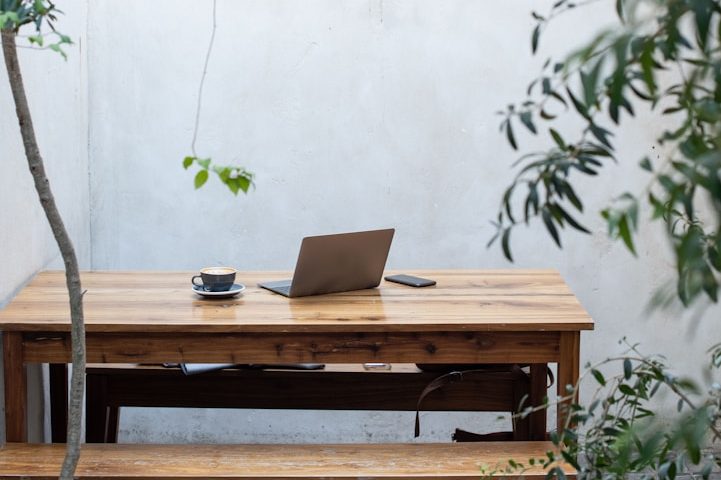 Laptop Kaffeetasse und Smartphone auf einem Holztisch in einem schlichten Innenhof