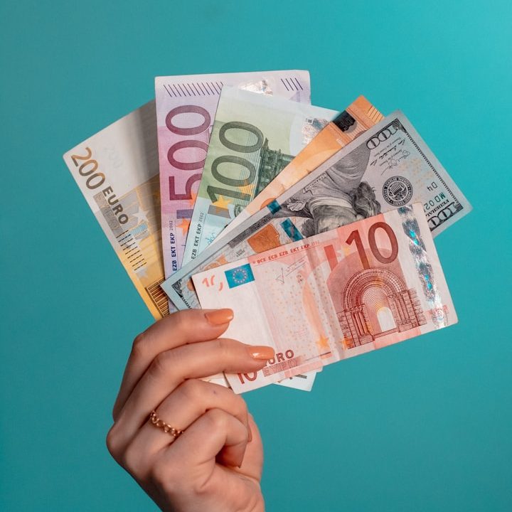 Weibliche Hand hält aufgefächerte Euro- und Dollarscheine