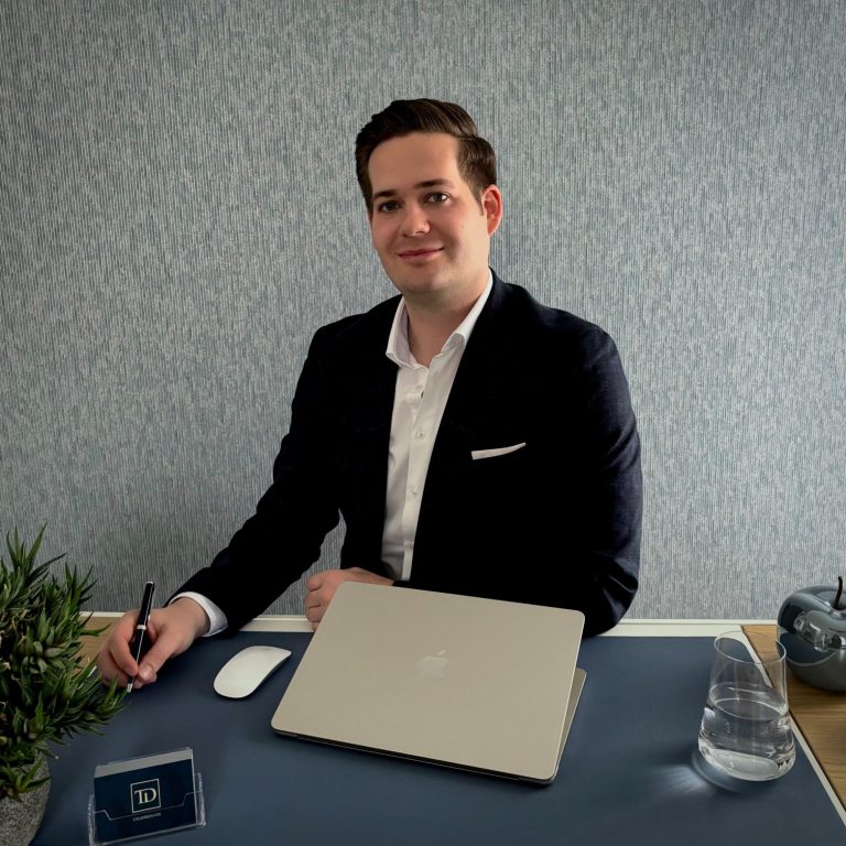 Steuerberater Tim Dahlke blickt am Schreibtisch lächelnd in die Kamera